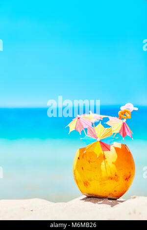 Coconut with colorful umbrellas and straws on a beach, summer fun holiday concept, selective focus, space for text. Stock Photo