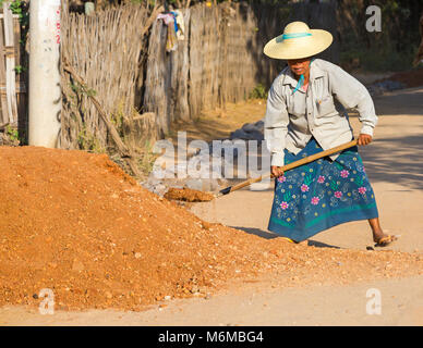 Villagers undertake manual road construction work at West Phwar Saw Village, Bagan, Myanmar (Burma), Asia in February - woman shovelling gravel Stock Photo