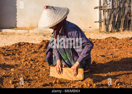 Villagers undertake manual road construction work at West Phwar Saw Village, Bagan, Myanmar (Burma), Asia - woman levelling using piece of wood Stock Photo