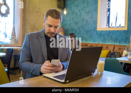 Businessman using smartphone and laptop while sitting at the table in cafe Stock Photo