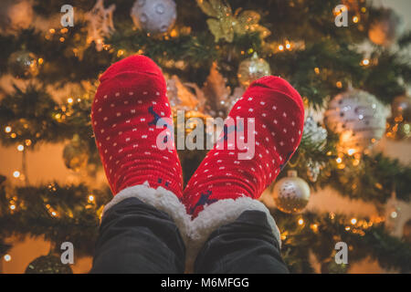Close up of feet wearing red Christmas socks against decorated Christmas tree background Stock Photo