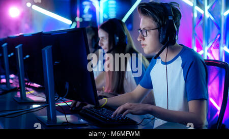 Team of Professional Cybersport Gamers Playing Video Games on a Cyber Games Tournament. Girls and Boys Have Headphones On, Arena is Lit with Neon Stock Photo