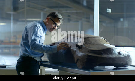 Chief Automotive Designer with Rake Sculpts Futuristic  Car Model from Plasticine Clay. He Works in a Special Studio Located In a Large Car Factory. Stock Photo