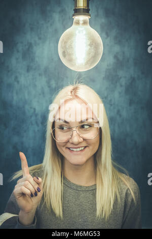 Happy thoughtful woman with light bulb above head isolated on blue wall background. Thinking and idea concepts. Stock Photo