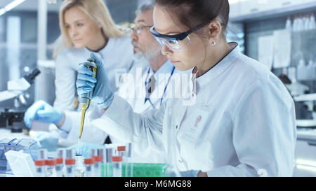 Team of Research Scientists Working With Personal Computer, Analysing Test Trial New Generation Drug Data and Using Micropipette for Filling Test Tube Stock Photo