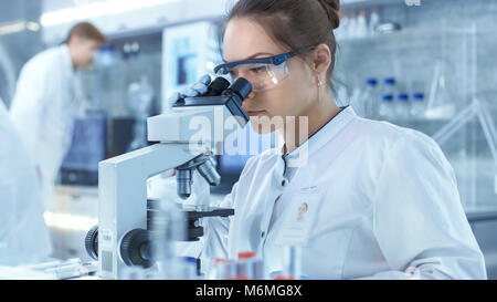 Medical Research Scientists Looking at Samples Under Microscope. She Works in a Bright Modern Laboratory. Stock Photo