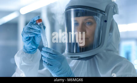 Medical Virology Research Scientist Works in a Hazmat Suit with Mask, Inspects Test Tube with Isolated Virus String from Refrigerator Box. Stock Photo