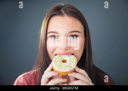 Pretty teenage girl holding and taking a bite out of a donut.