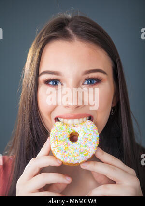 Pretty teenage girl holding and taking a bite out of a donut.