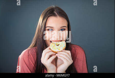 Pretty teenage girl holding and taking a bite out of a donut.
