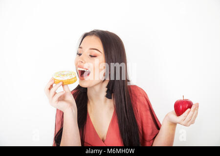 Pretty teenage girl taking a bite out of a donut and holding an apple in her hand.