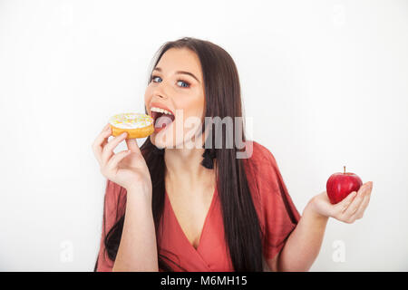 Pretty teenage girl taking a bite out of a donut and holding an apple in her hand.