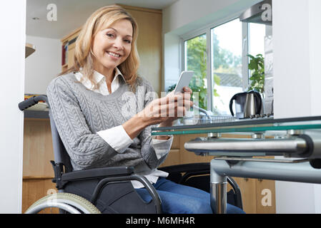 Portrait Of Disabled Woman In Wheelchair Using Mobile Phone At Home Stock Photo