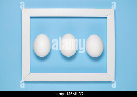 Flat lay of white egg in wooden frame on blue background minimal concept. Stock Photo