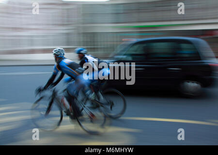 Panning shot of two cyclists photographed from behind in London. Black taxi in the background.