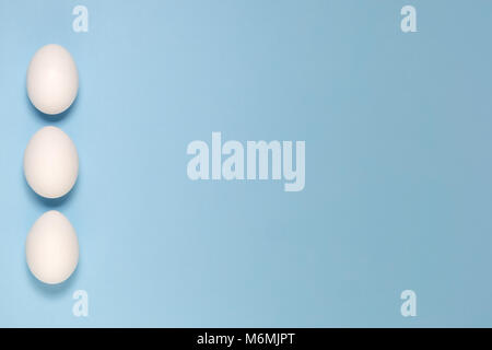 Three white eggs on plain pastel blue background. Minimal concept. Stock Photo