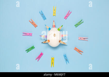 White egg with thorns made of colorful pencils and clothespins in circle against blue pastel background. Easter art minimal concept Stock Photo