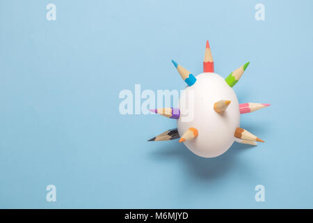 White egg with thorns made of colorful pencils against blue pastel background. Easter minimal concept. Stock Photo