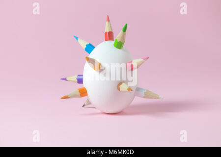 White egg with thorns made of colorful pencils against pink pastel background. Easter minimal concept. Stock Photo