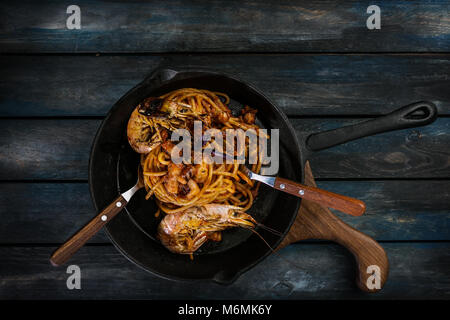 Spaghetti. Pasta with seafood on a hot frying pan with a spoon and fork on a colored wooden background. Top view Stock Photo