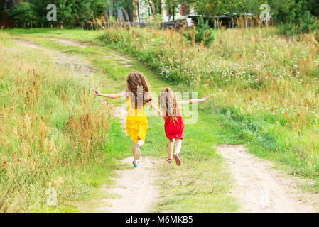 Two little sisters running and playing on the road in countryside on a warm summer sunset. Cute little girls Stock Photo