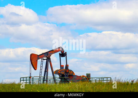 Colorful pump jack on oil well - low horizon on prairie with green grass and wild flowers - big blue cloudy sky - room for text Stock Photo