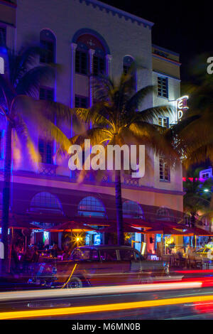 Ocean Drive in Miami at night with vibrant street colours. Cars passing by creating lines of light during long exposure. Palms, hotel in background.