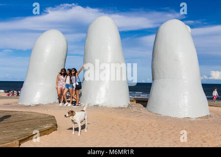 Punta Del Este, Uruguay - February 28th, 2018: Three young women taking photos and sefies at La Mano, the sculpture made by Mario Irarrazabal, Playa L Stock Photo