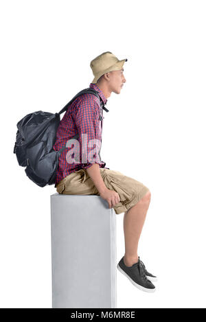 Side view of asian backpacker man with hat sitting isolated over white background Stock Photo