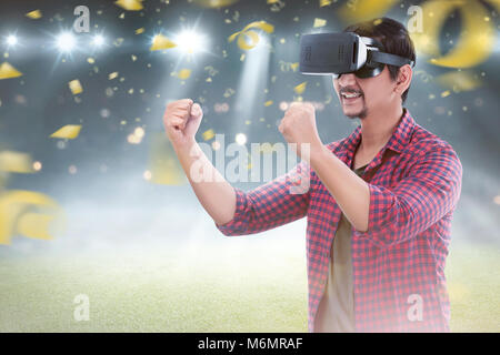 Young asian man with virtual reality enjoying the football game with confetti background Stock Photo
