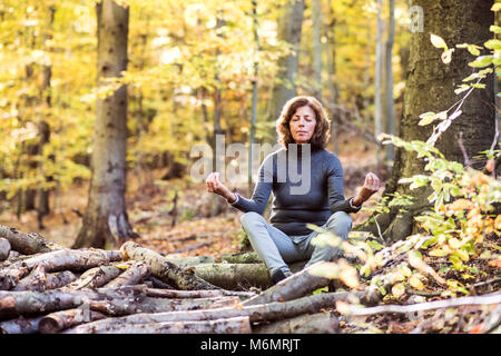 Senior woman meditating in an autumn forest. Stock Photo