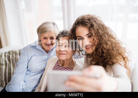 A teenage girl, mother and grandmother with smartphone at home. Stock Photo