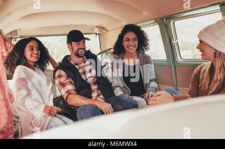 Multiethnic friends on roadtrip travelling together in a van. Group of man and women sitting inside a van and laughing. Stock Photo