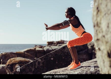 Woman runner doing stretching exercises. Woman doing warm up stretches on rocks at the beach. Stock Photo