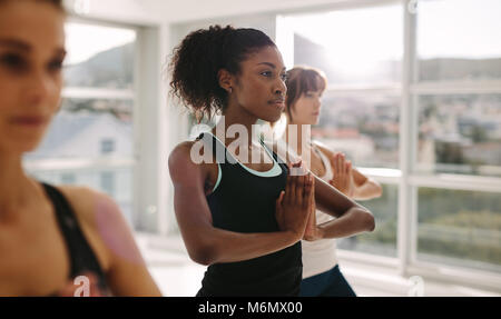 Women stretching and practices yoga in class. Healthy female doing yoga workout in fitness studio. Standing with hands joined. Stock Photo