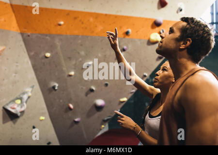 Female instructor giving instructions to a man on wall climbing. Man learning the art of rock climbing at an indoor climbing centre. Stock Photo