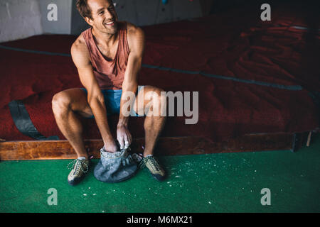 Smiling man at a wall climbing gym applying magnesium chalk powder on hands from a bag. Stock Photo