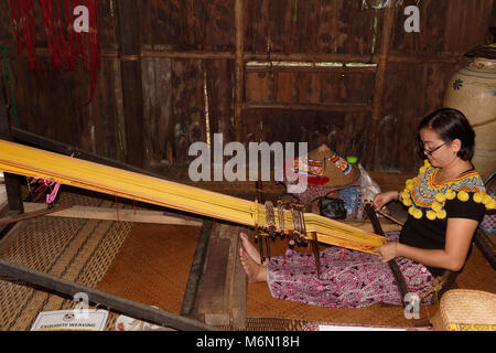 Woman in traditional dress weaving on a loom, Iban Longhouse, Sarawak Cultural village, Kuching, Borneo, Malaysia Stock Photo