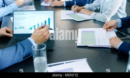 Shot of the Business Meeting Room Table with People Sharing Documents with Pie Charts and Statistics, Tablet and Laptop Screens. Stock Photo