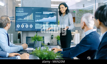 Beautiful Businesswoman Gives Report/ Presentation to Her Business Colleagues in the Conference Room, She Shows Graphics, Pie Charts and Graphs Stock Photo