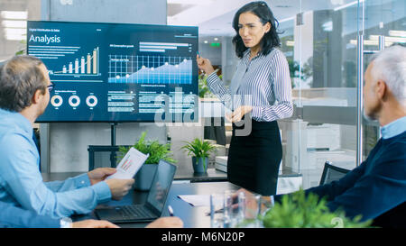 Beautiful Businesswoman Gives Report/ Presentation to Her Business Colleagues in the Conference Room, She Shows Graphics, Pie Charts and Graphs Stock Photo