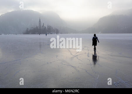 Frozen lake Bled, Slovenia in winter. People walk to the island and skate on ice Stock Photo