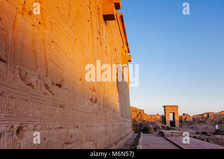 Bas reliefs outside the Temple of Hathor with one of the compound´s gateways in background at sunset. Dendera, Egypt Stock Photo