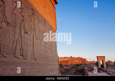 Bas reliefs outside the Temple of Hathor with one of the compound´s gateways in background at sunset. Dendera, Egypt Stock Photo