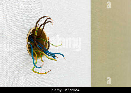Several exposed electrical copper wires protruding from a whitewall. Stock Photo