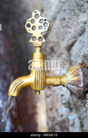 Public metal yellow faucet fountain with drinking clear water flowing in old traditional city Stock Photo