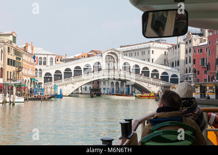 Tourists on a Vaporetto travelling up the Grand Canal, Rialto Bridge, Venice, Italy in winter with snow on the roofs, first person POV over the bow Stock Photo