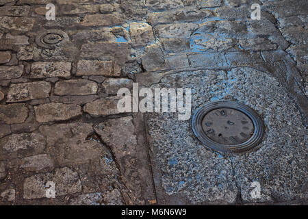 Close up of wet old stone floor with puddles and water supply covers Stock Photo