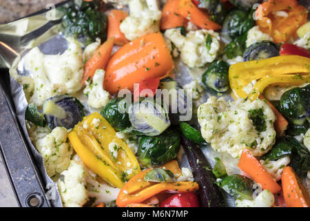 Foiled lined baking sheet filled with raw carrots, cauliflower, brussels sprouts, baby bell peppers coated in oil and spices to be roasted in the oven Stock Photo