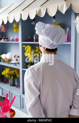 Rear view of the chef in the kitchen in the restaurant. In a white robe and a cap. Stock Photo